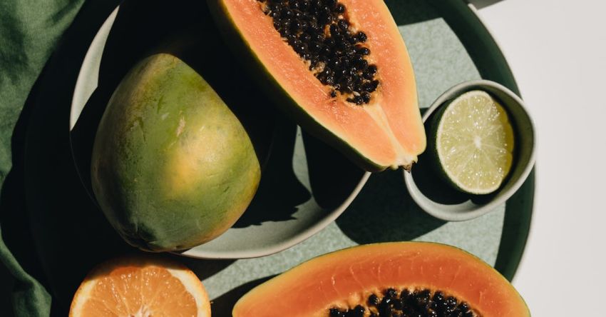 Diet Tips - Top view of halves of ripe papaya together with oranges and limes placed on green round dishes and green fabric on white background